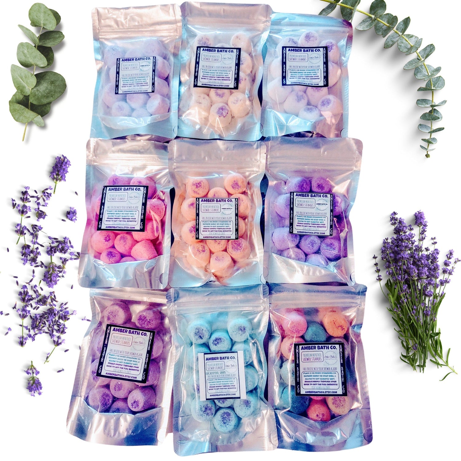 A variety of different colored shower steamers in bags with Eucalyptus and Lavender in the background