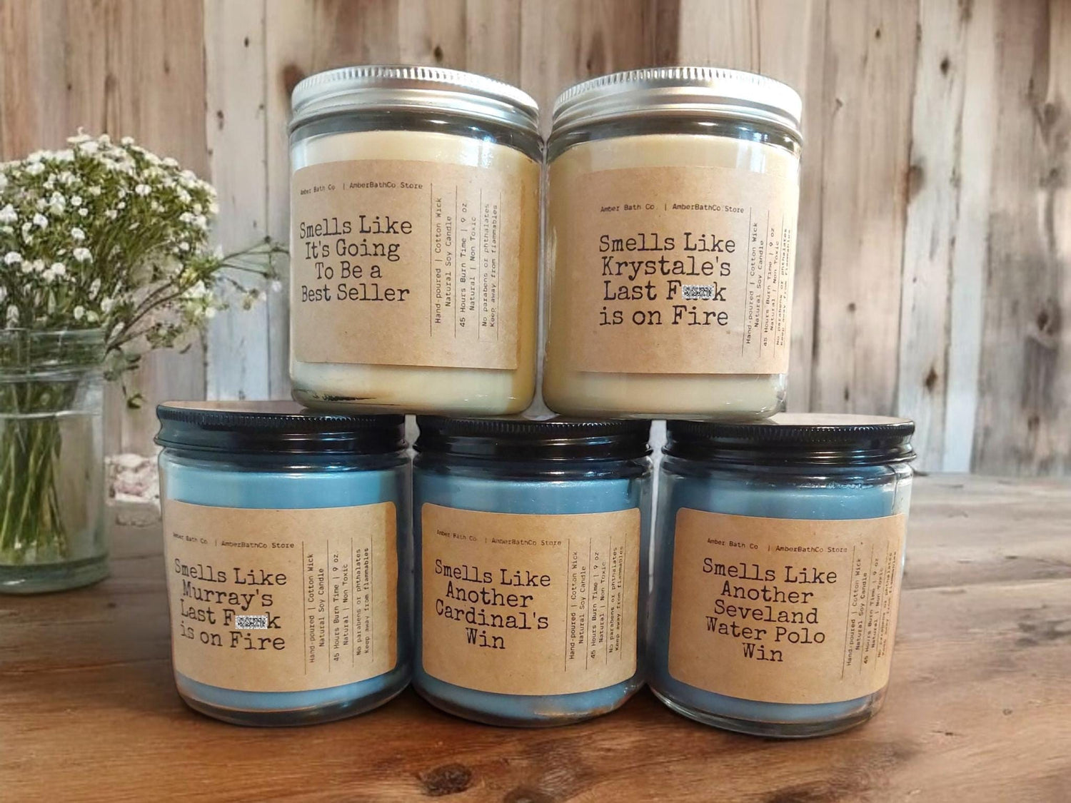 Five 9 oz soy candles on a rustic wooden table. Craft paper label with text such as "Smells Like It's Going to Be a Best Seller," and "Smells Like Another Cardinal's Win."