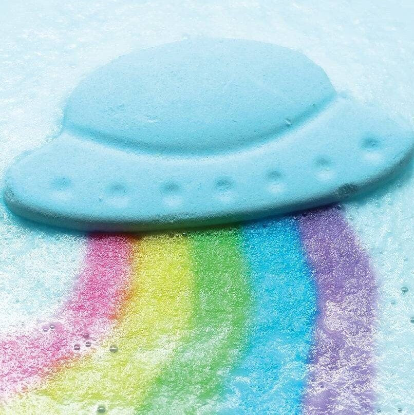 A blue spaceship bath bomb shooting out rainbows of colors in foamy water.